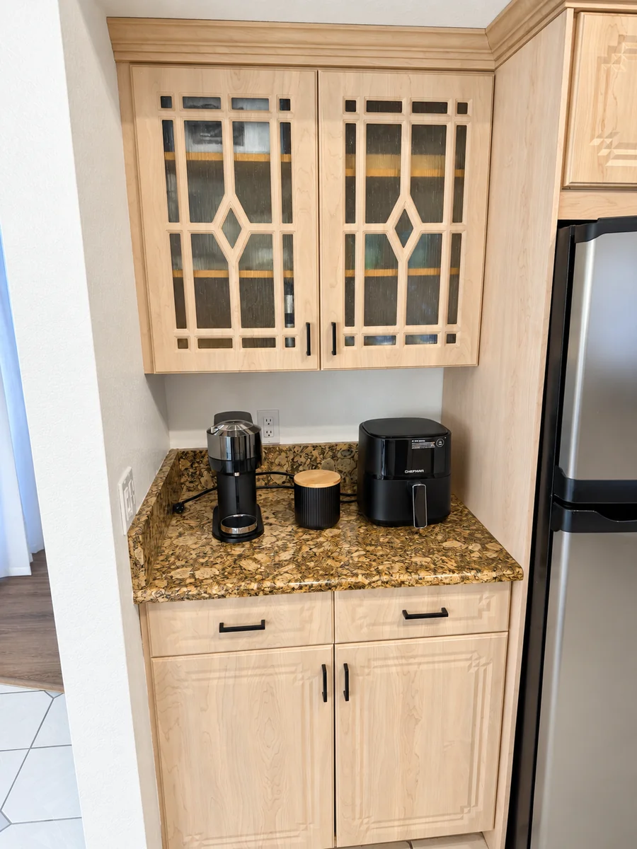 Coffee machine and air fryer on a granite counter beneath light wood cabinets