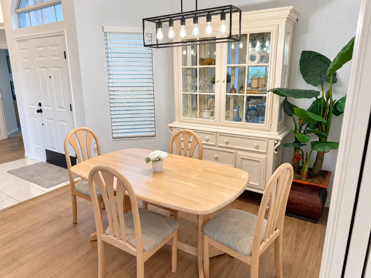 Wood dining table and chairs beneath a pendant light, beside a glass-front cabinet