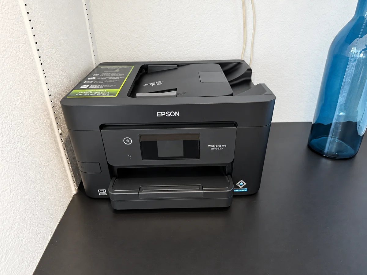 Black Epson printer on a shelf beside a blue vase