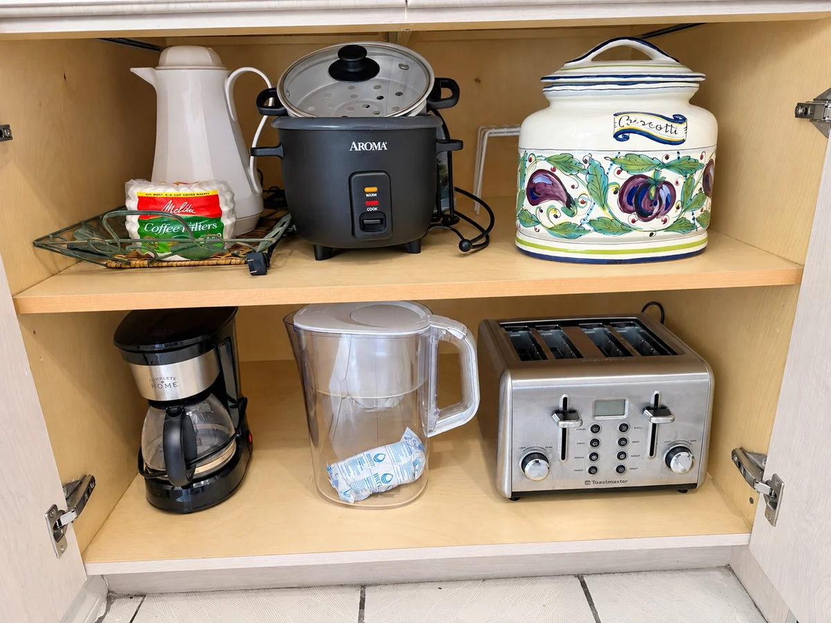 Cabinet shelves with a rice cooker, coffee maker, toaster, and water pitcher